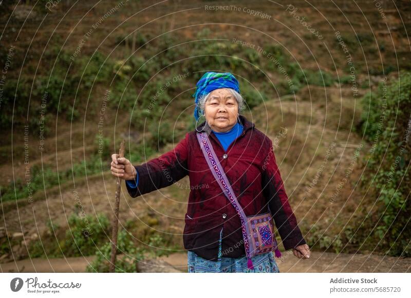 Cheerful senior woman with strap bag and stick stand warm clothes scarf cheerful positive smile countryside winter nature happy aged female joy lifestyle season