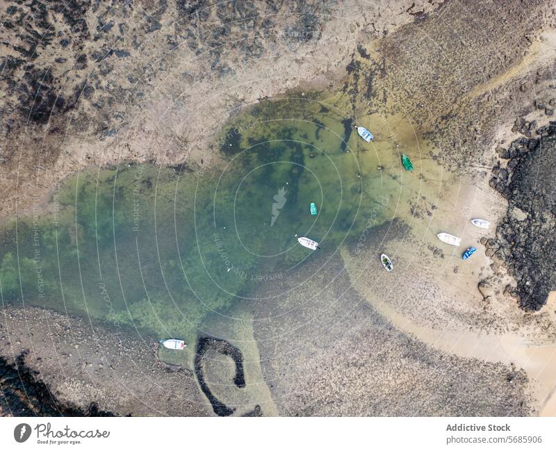 Top view of boats moored in a shallow cove with crystal-clear waters along the north coast of Fuerteventura, near Faro del Toston top view lighthouse El Cotillo