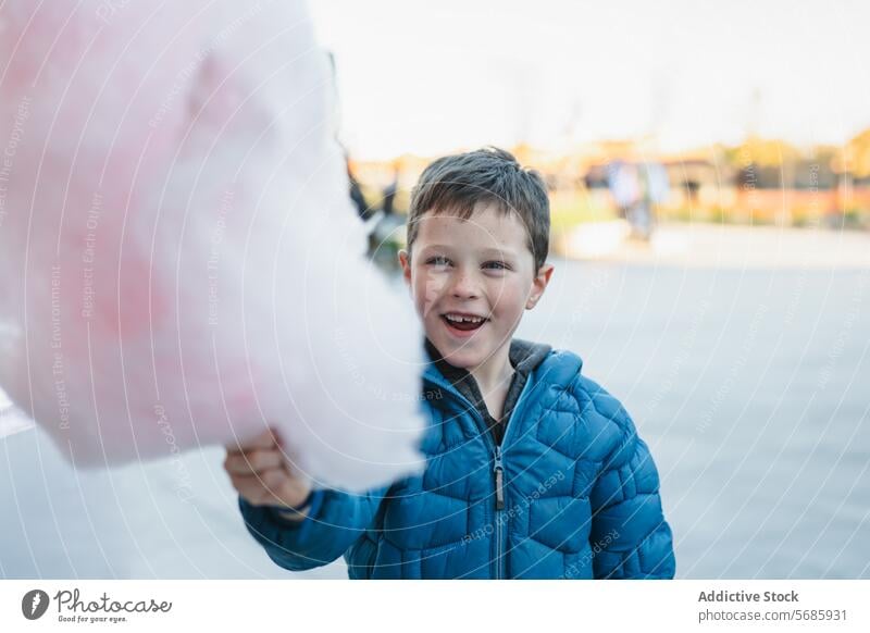 A cheerful young boy holding a large pink cotton candy in an outdoor setting smile joy treat sweet sugary confection fluffy happy enjoyment fun indulgence snack