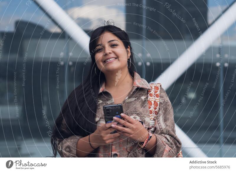 Young woman using smartphone to against glass building on street smile positive happy casual city portrait bracelet device gadget optimist urban female daytime