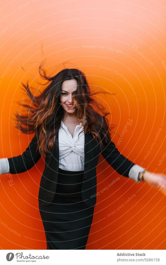 Joyful woman with dynamic hair against orange backdrop smiling vibrant madrid spain carefree happiness professional attire wall joyful female brunette flick