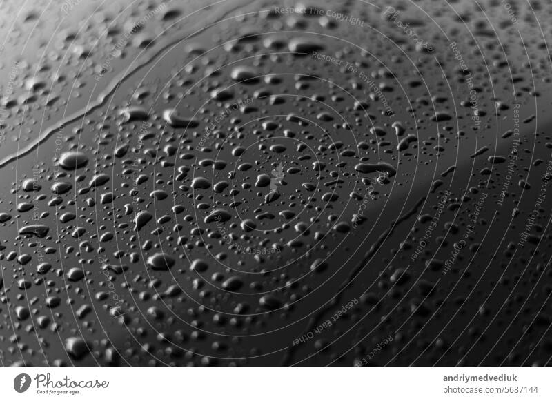 Rain or water drops different size on a black shiny car hood surface. Water droplets on dark iron surface and texture. Abstract background and water texture for design.