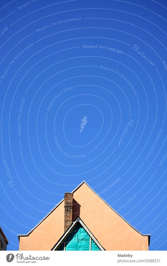 Pointed gable of an old building in pastel colors with an old brick chimney in front of a blue sky in the sunshine in the Sachsenhausen district of Frankfurt am Main in Hesse