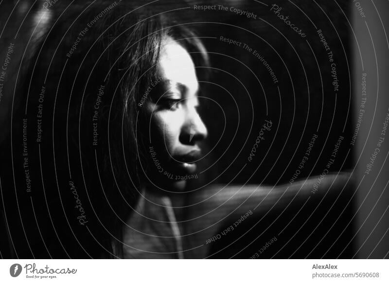 Young, long-haired woman behind transparent curtain/net stands illuminated in semi-darkness and looks to the side Woman Young woman Long-haired Dark Black