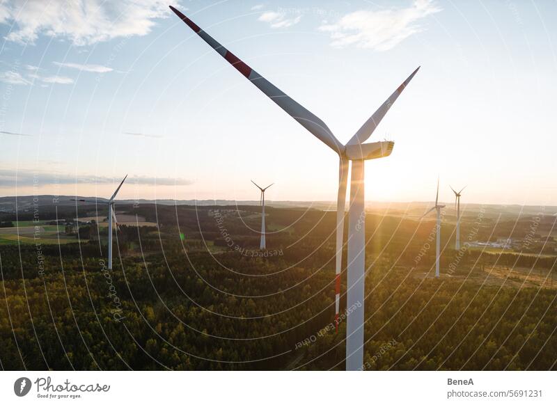 Wind turbines in a hilly forest in front of a partly cloudy, but sunny sky are seen from an aerial view during sunset Aerial Clean Cleantech Country Countryside