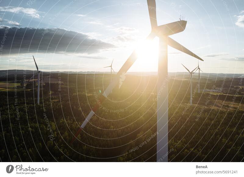 Wind turbines in a hilly forest in front of a partly cloudy, but sunny sky are seen from an aerial view during sunset Aerial Clean Cleantech Country Countryside