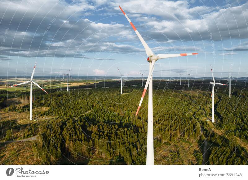 Wind turbines in a hilly forest in front of a partly cloudy, but sunny sky are seen from an aerial view during sunset Aerial Clean Cleantech Country Countryside