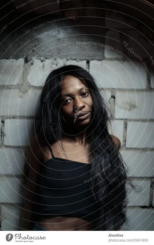 Young, long-haired, slim woman stands in front of a wall of white bricks and into the camera Woman Young woman Long-haired Dark Feminine Human being