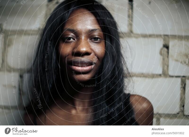 Young, long-haired, slim woman stands in front of a wall of white bricks and into the camera Woman Young woman Long-haired Dark Feminine Human being