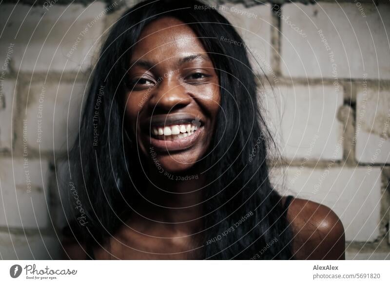 Young, long-haired, slim woman stands in front of a wall of white bricks and laughs - great joy Woman Young woman Long-haired Dark Feminine Human being