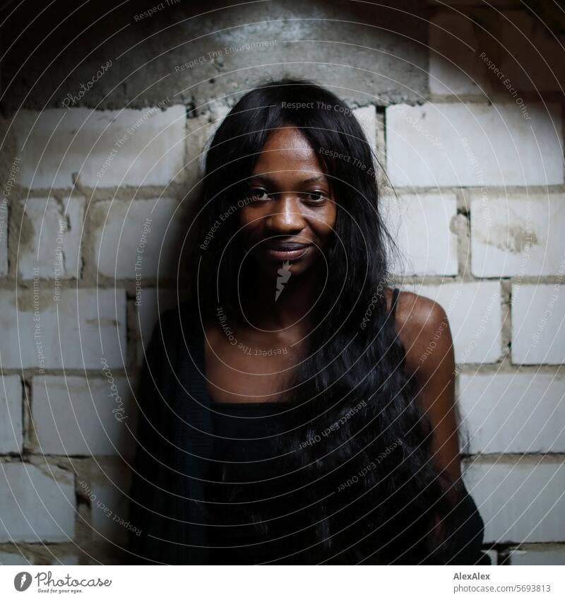 Young, long-haired, slim woman stands in front of a wall of white bricks and into the camera Woman Young woman Long-haired Dark Feminine Human being