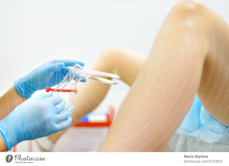 Gynecologist examines a patient laying on gynecological chair using medical vaginal speculum. Doctor takes a smear from a young woman cervix. Diagnosis of diseases.