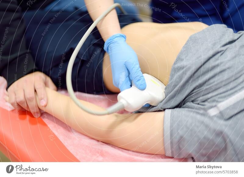 Doctor making abdominal ultrasound for boy using scanner machine. Female doc runs ultrasound sensor over patient tummy. Mother supports son during diagnosis examination of internal organs