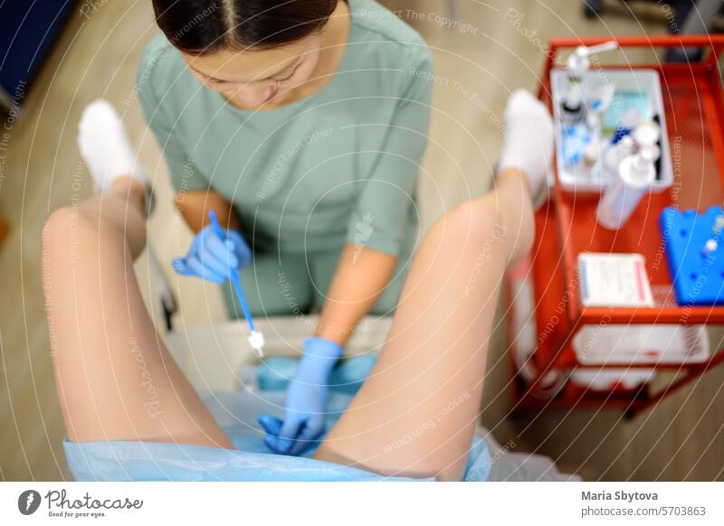 Gynecologist examines a patient laying on gynecological chair using medical vaginal speculum. Doctor takes a smear from a young woman cervix. Diagnosis of diseases.