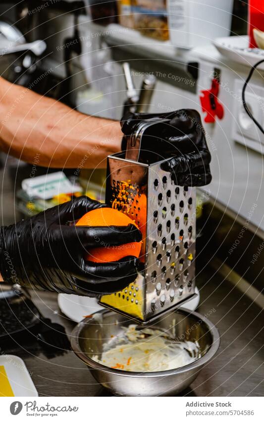 Chef grating orange zest into metal bowl in kitchen chef culinary recipe professional black glove cooking preparation food ingredient fruit utensil grater work