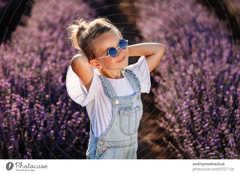 adorable child girl in lavender field on sunset. smiling kid in sunglasses, jeans jumpsuit is having fun on nature on summer day. Family day, vacation, holiday.International Children's Day,