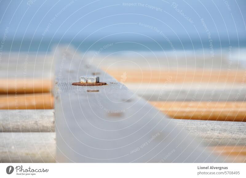 Focus on a Rusty nut of an old wood plank with a very shallow deep of field bolt rusty close-up sea sky gray blue orange fence beach day light lines outside