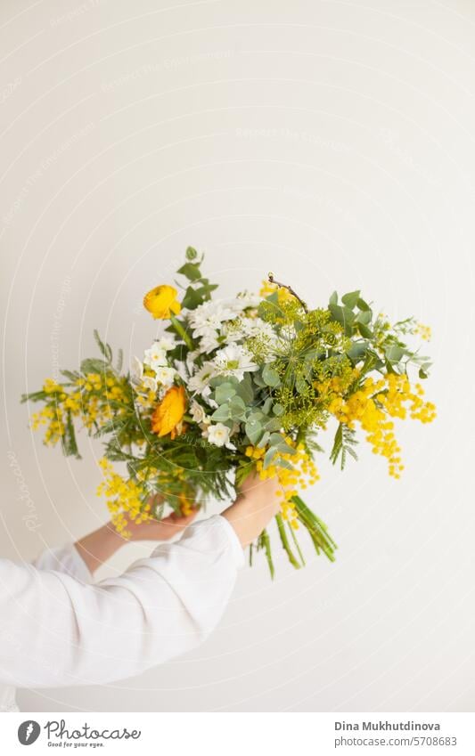 hand holding beautiful bouquet with yellow mimosa spring flowers, ranunculus and eucalyptus leaves. Fresh elegant home decor. Florist work. salon vase florist