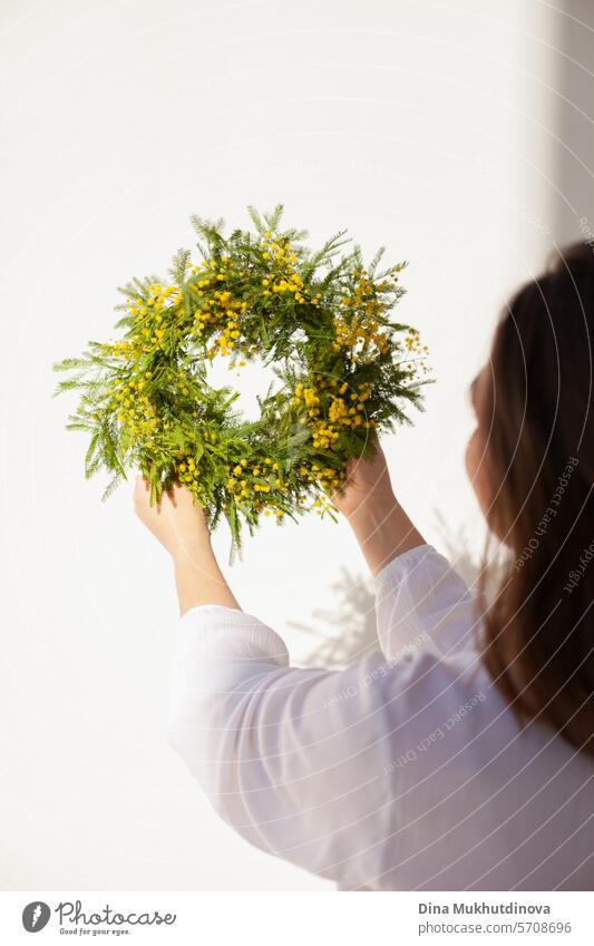 female florist holding beautiful wreath with yellow mimosa spring flowers. Fresh elegant home decor. Florist work. salon vase floristry eucalyptus leaves leaf