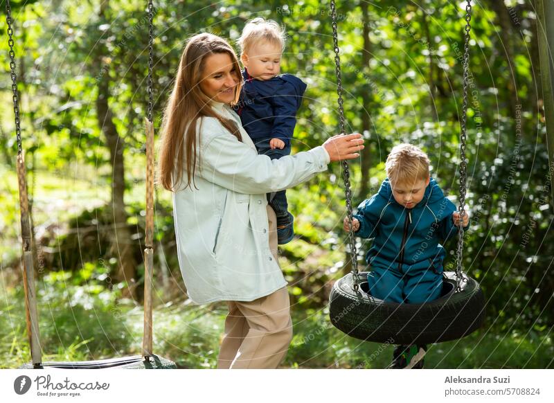 The mother with two children is having a fun time at the playground. The mother is swinging her children on the swings. active activity baby boy care caucasian