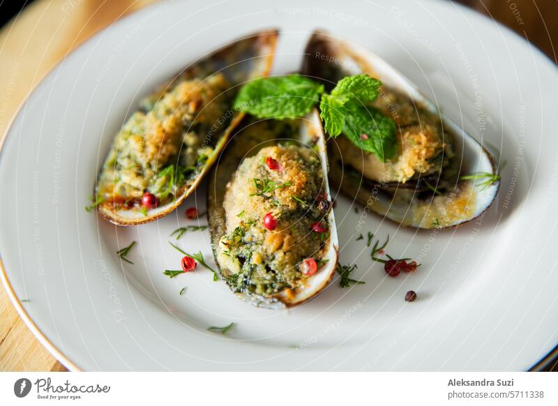 Cooked green mussels with butter, greens and seasoning. Dinner served on white porcelain plate. Kitchen counter appetizer background bake catch cheese clams