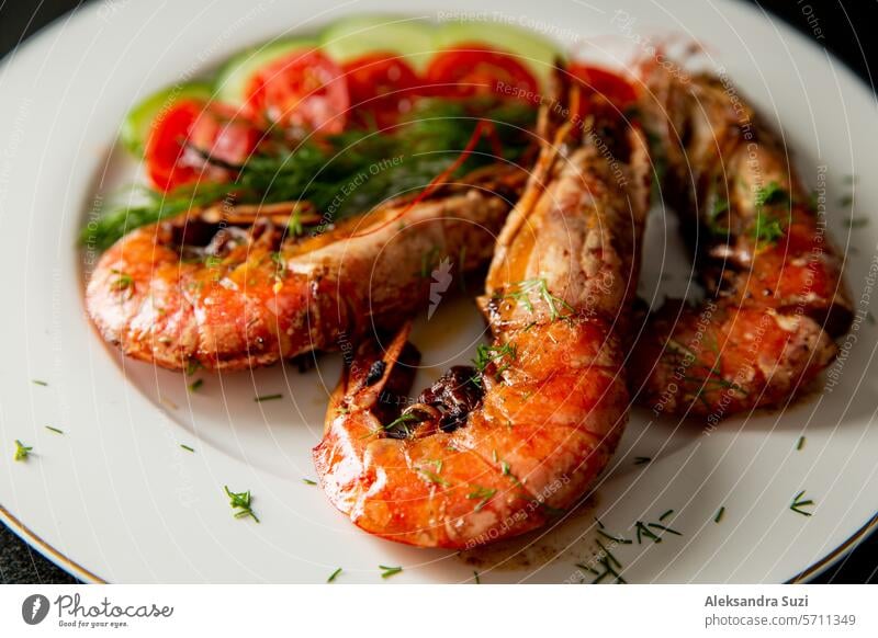 Cooked langoustine served on plate with cherry tomatoes and greens. Hand squeezing lemon juice on top. appetizer black board butter chopping closeup cooking