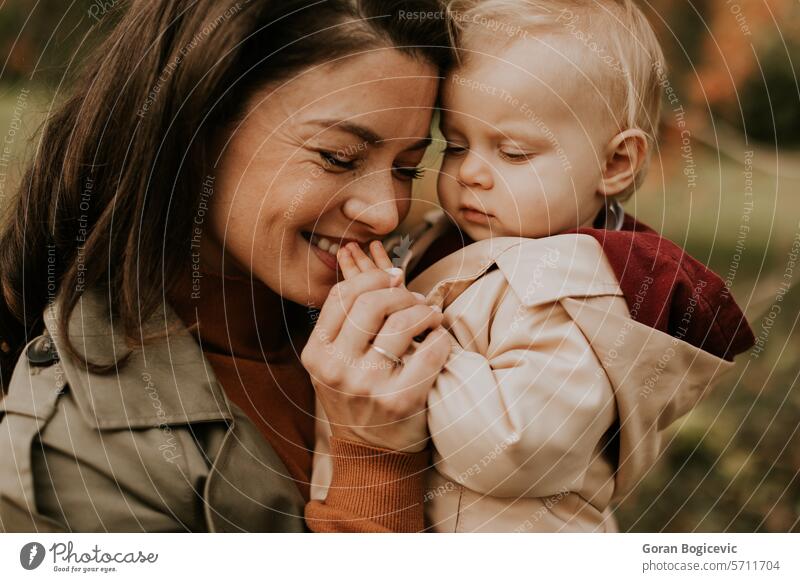 Young woman holding cute baby girl in the autumn park small caucasian mother outside daughter child little love happiness together family play mom smile season