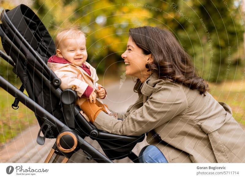 Young woman with cute baby girl in baby stroller at the autumn park adorable adult care caucasian child childhood daughter fall family female foliage happiness