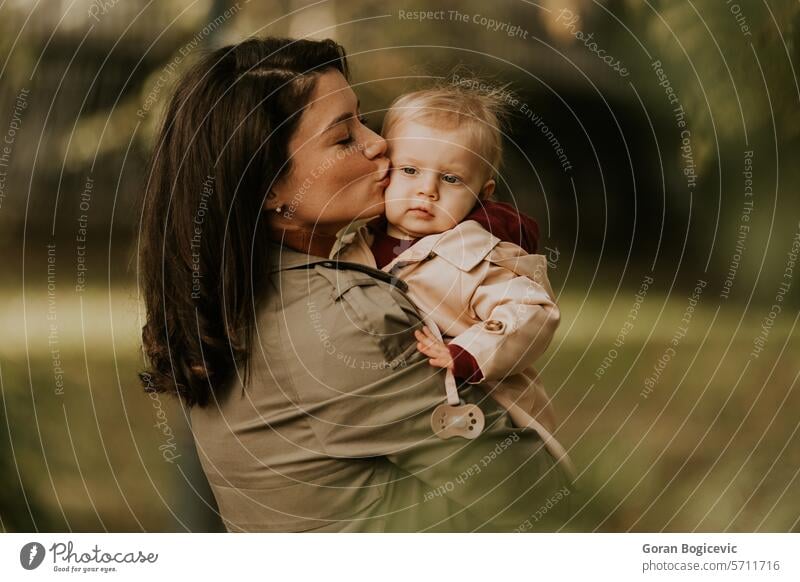 Young woman holding cute baby girl in the autumn park small caucasian mother outside daughter child little love happiness together family play mom smile season