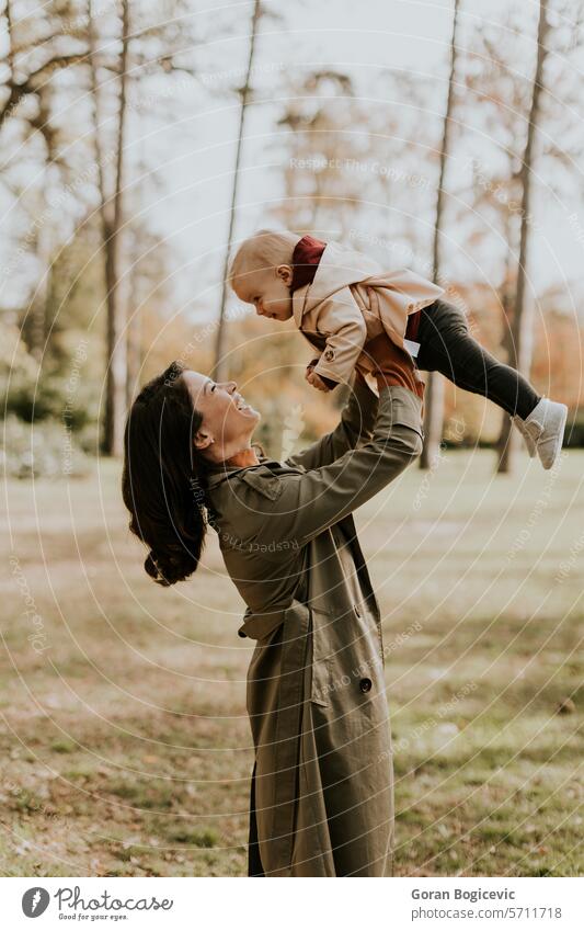 Young woman holding cute baby girl in the autumn park small caucasian mother outside daughter child little love happiness together family play mom smile season