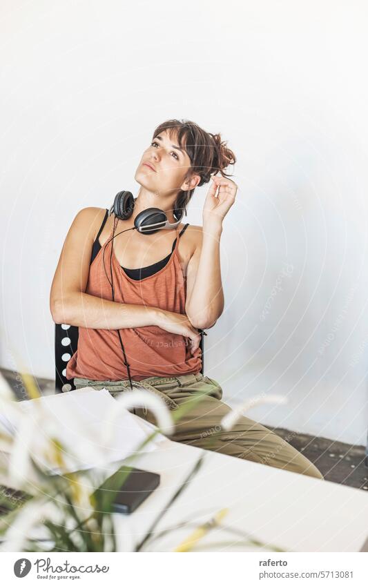 A young woman takes a break from her creative work reflection headphones pen thought project contemplative pause casual inspiration pondering relaxed thinking