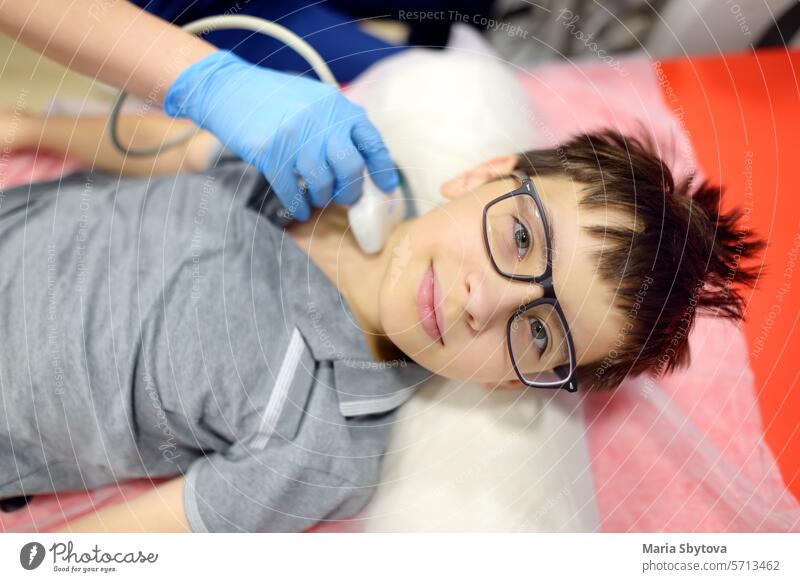 Doctor making ultrasound of the thyroid gland for boy using scanner machine. Female doc runs ultrasound sensor over patient neck for scanning of the thyroid gland and lymph nodes.