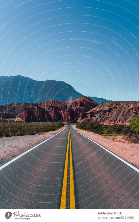 Straight road stretching towards red rock formations under a vast blue sky in the Los Castillos area of northern Argentina straight desert landscape travel