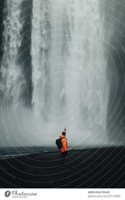 Unrecognizable man in orange jacket facing majestic Skogafoss waterfall iceland travel skogafoss mist adventure nature outdoor male backpack exploration tourist