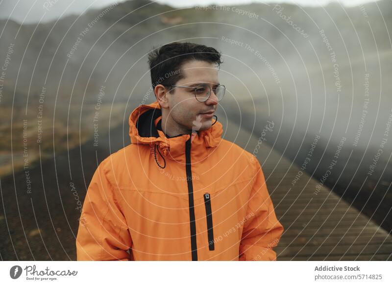 Man in orange jacket exploring misty Icelandic terrain iceland travel adventure man male raincoat fog volcanic landscape outdoors exploration wanderlust nature