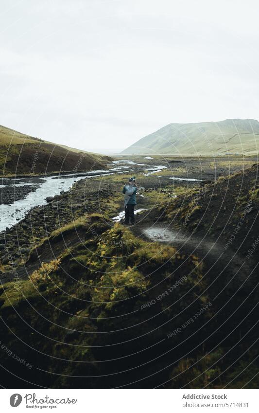 Man exploring vast Icelandic valley by river iceland travel exploration man male green hills serenity wanderlust journey nature outdoors landscape adventure