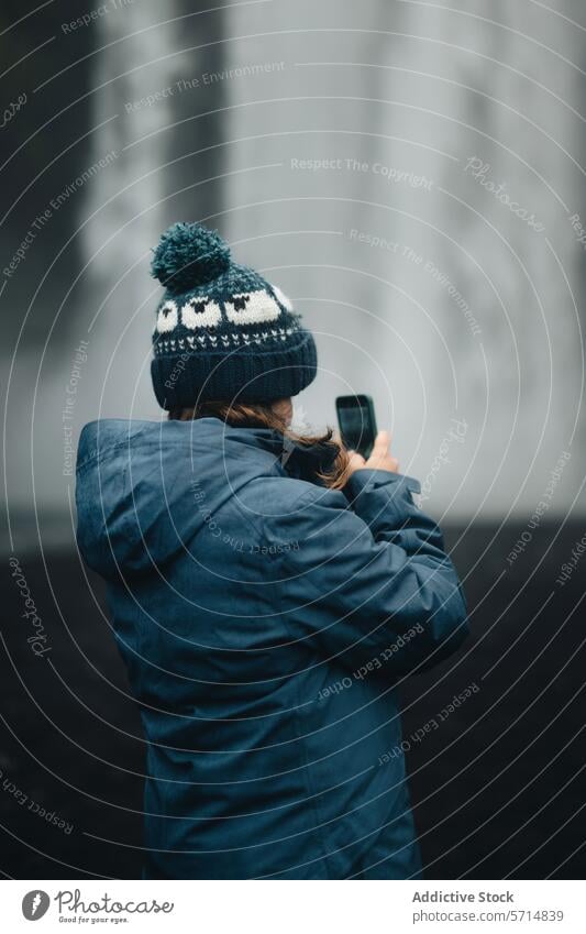 Woman capturing the misty Skógafoss Waterfall with smartphone iceland skógafoss waterfall female tourist photography adventure travel woman nature scenic