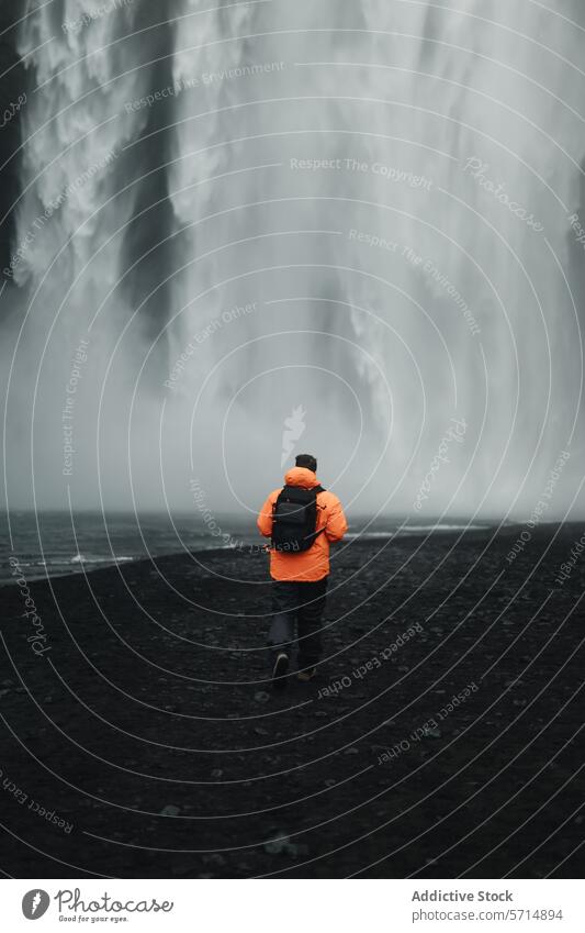 Man exploring the majestic Skogafoss waterfall in Iceland iceland skogafoss male man adventure explorer travel nature volcanic beach wonder backpack