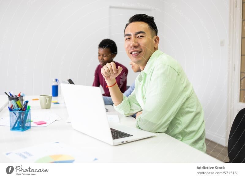 Diverse team during a collaborative office meeting asian man smiling work atmosphere diverse colleagues casual shirt green business laptop communication