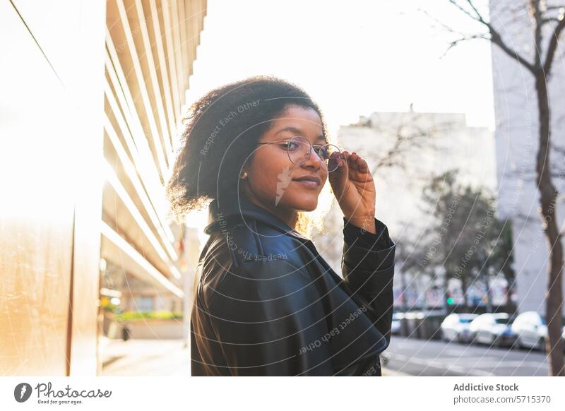 Stylish woman with glasses stands on a city sidewalk at dusk, with the warm glow of the setting sun illuminating her face Woman sunset style stylish coat winter