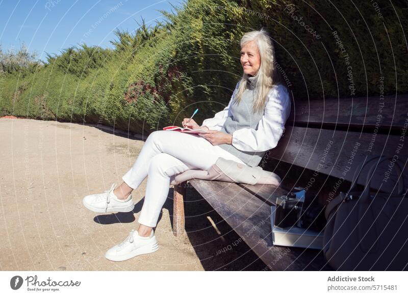 Woman in her 50s writing in a notebook on a park bench with a camera beside her, enjoying a creative moment leisure creativity lifestyle mature relaxation sunny