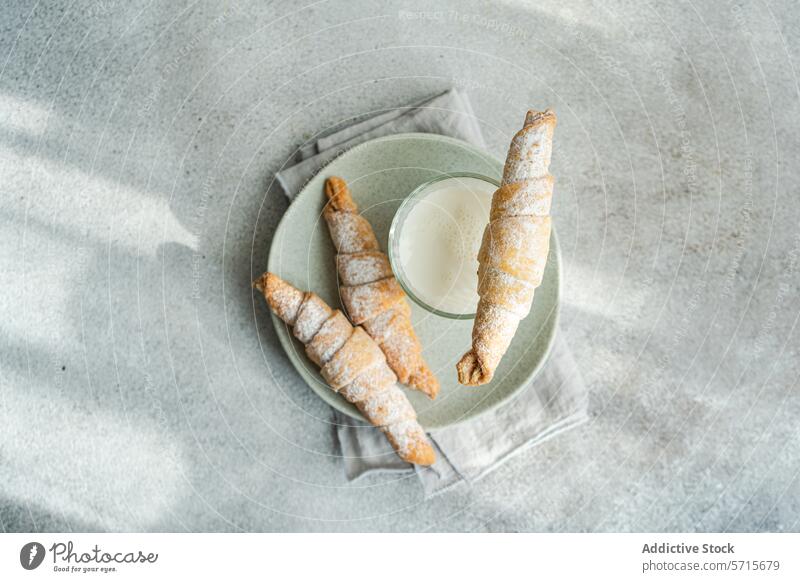 Top view of homemade pastry cones filled with jam and sprinkled with powdered sugar, alongside a glass of milk on a ceramic plate, set on a textured grey surface