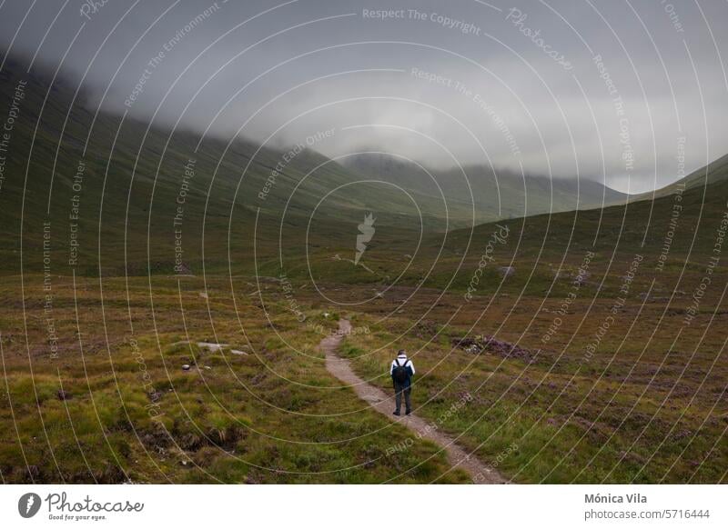 A man walks along a mountain path in the Glencoe Mountains on a day with dramatic skies from the Glencoe Lookout mountains Glencoe view point scottish highlands