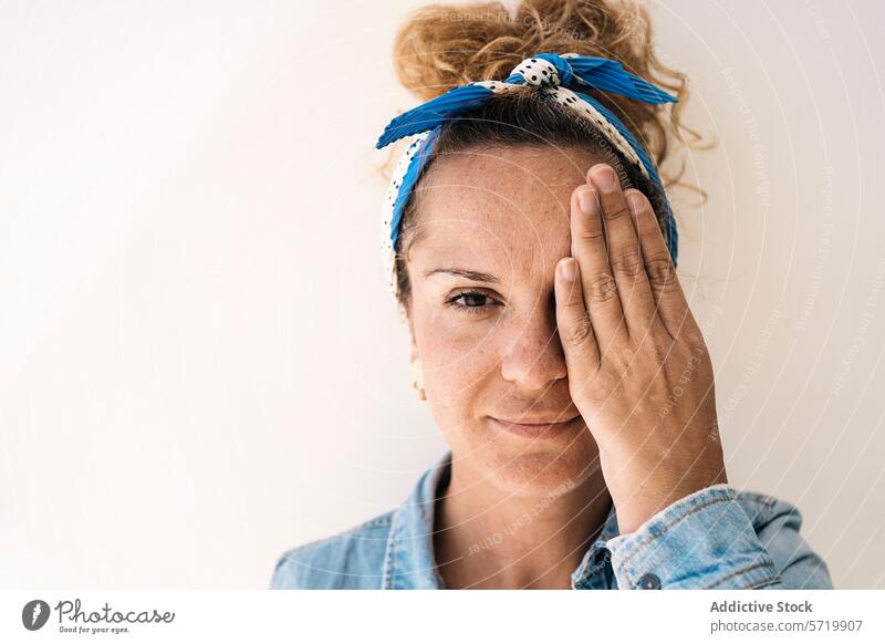 A portrait of a reflective woman with a headscarf and glasses, covering half of her face with a hand that reveals a surgical absence of a thumb thoughtful