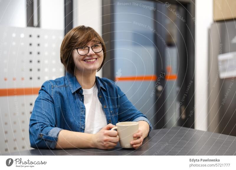 Young woman on a coffee break in the office kitchen smiling positive emotion sitting drinking cup of coffee business employee female job people profession