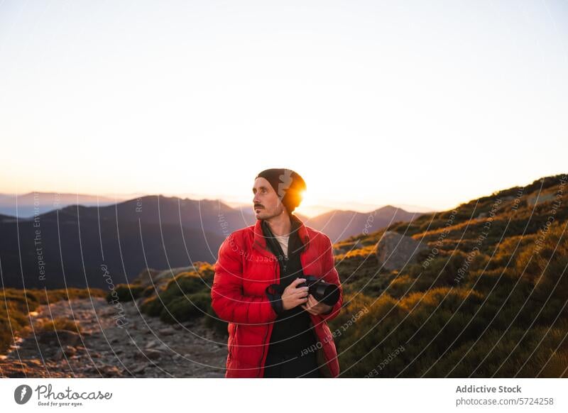 Photographer capturing sunset in mountain landscape photographer camera man red jacket beanie backlight sun rays outdoor adventure nature hobby photography