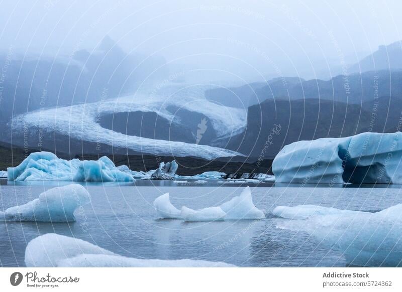 Icebergs drift in the hushed waters of a glacial lagoon with Vatnajökull's ice sheet veiled in mist, capturing Iceland's ethereal beauty twilight mystique