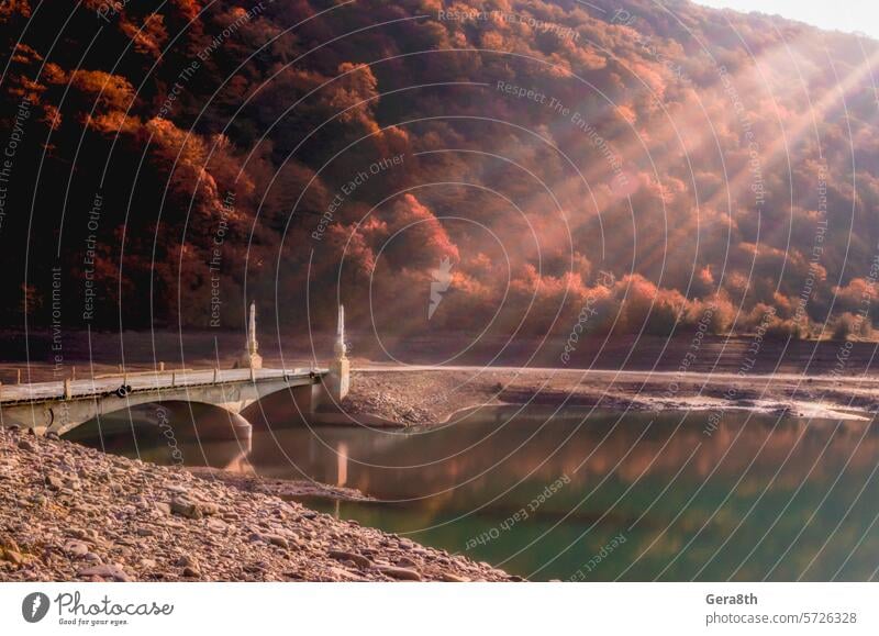 old vintage stone bridge over the river on a background of mountains with trees Caucasus Georgia Sakartwell autumn green hill lake landscape lens flare light