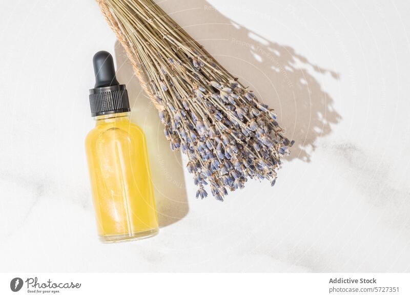 A clear bottle filled with golden-colored oil essence lies next to a bouquet of dried lavender, suggesting organic beauty and relaxation skincare glass