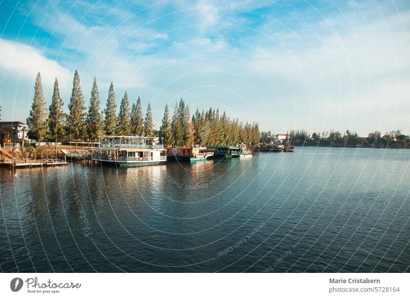 A serene river scene with boats docked by a pier and trees lining the shore under a partly cloudy sky in Kampot, Cambodia kampot cambodia tourist attraction